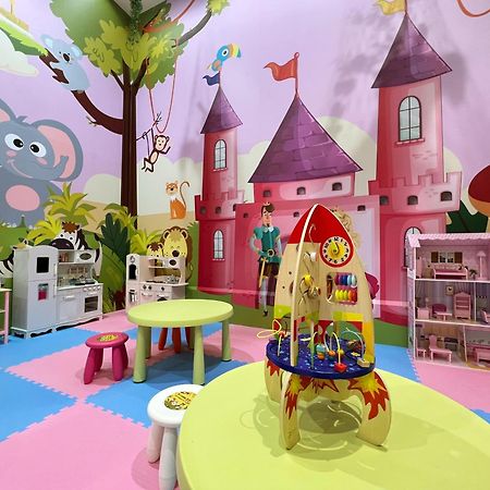 Evergreen Laurel Hotel - טאיצ'ונג מראה חיצוני תמונה The photo shows a colorful children's playroom designed with a whimsical theme. The walls are painted in bright colors and feature a cartoon-style mural of a pink castle with purple towers and a smiling cartoon elephant. The room is filled with playf