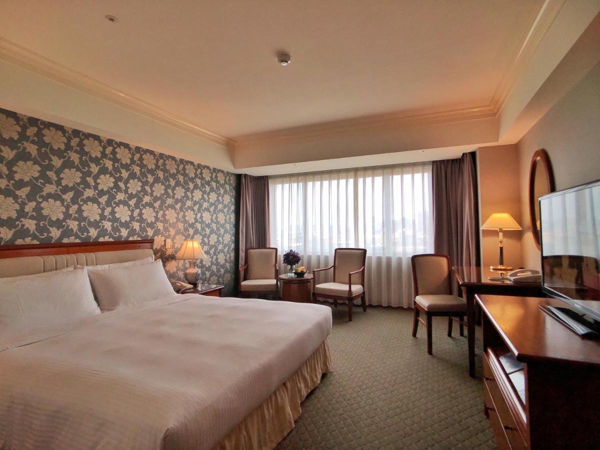 Evergreen Laurel Hotel - טאיצ'ונג מראה חיצוני תמונה The photo shows a well-appointed hotel room. It features a large bed with white bedding and a decorative headboard. The walls are adorned with a patterned wallpaper, possibly floral, adding a touch of elegance. There is a window with sheer curtains t