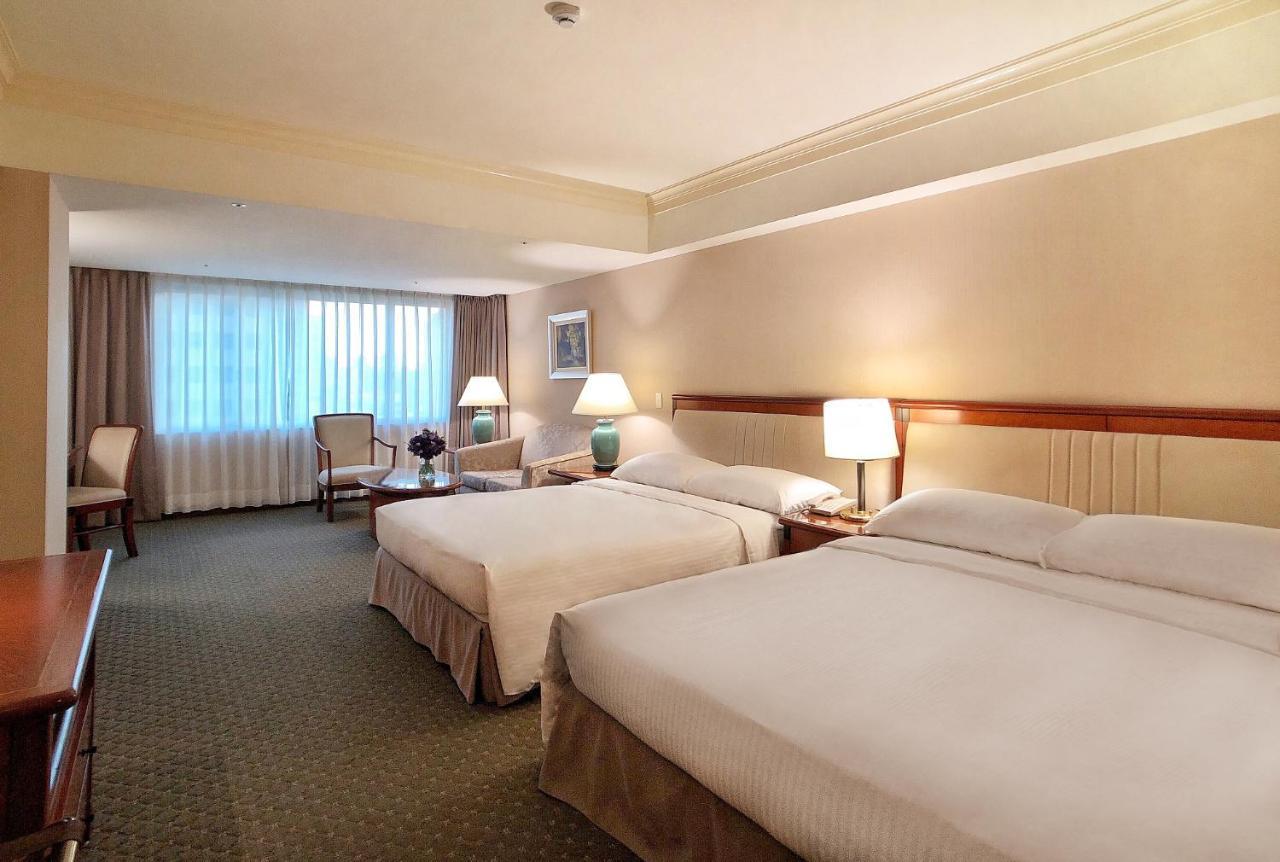 Evergreen Laurel Hotel - טאיצ'ונג מראה חיצוני תמונה The photo shows a hotel room featuring two queen-sized beds with white linens. The room is well-lit and has a warm, neutral color palette. There are bedside lamps on each side of the beds and a small table. To the side, there's a comfortable armchair