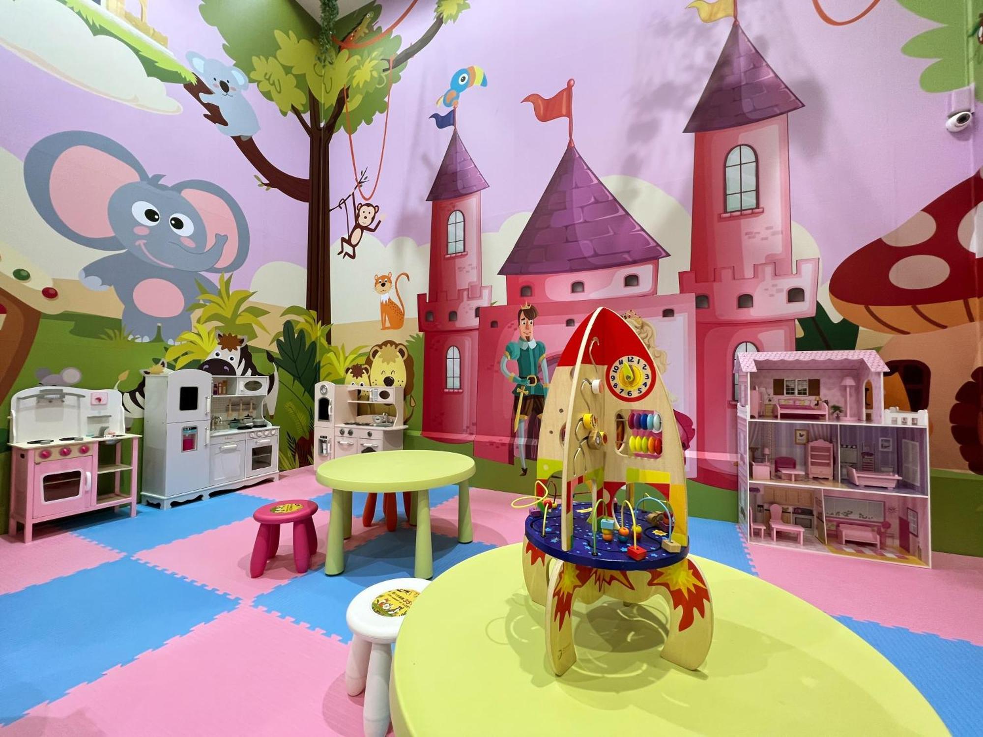 Evergreen Laurel Hotel - טאיצ'ונג מראה חיצוני תמונה The photo shows a colorful children's playroom designed with a whimsical theme. The walls are painted in bright colors and feature a cartoon-style mural of a pink castle with purple towers and a smiling cartoon elephant. The room is filled with playf