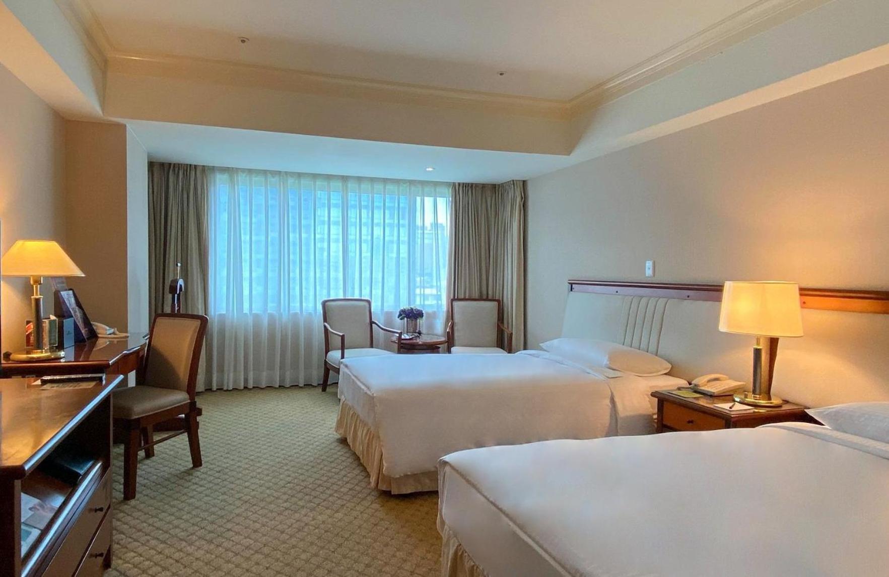 Evergreen Laurel Hotel - טאיצ'ונג מראה חיצוני תמונה The photo shows a hotel room featuring two single beds positioned near each other. There's a light-colored carpet on the floor and a large window with sheer curtains that allows natural light to fill the space. In the room, there are two chairs place