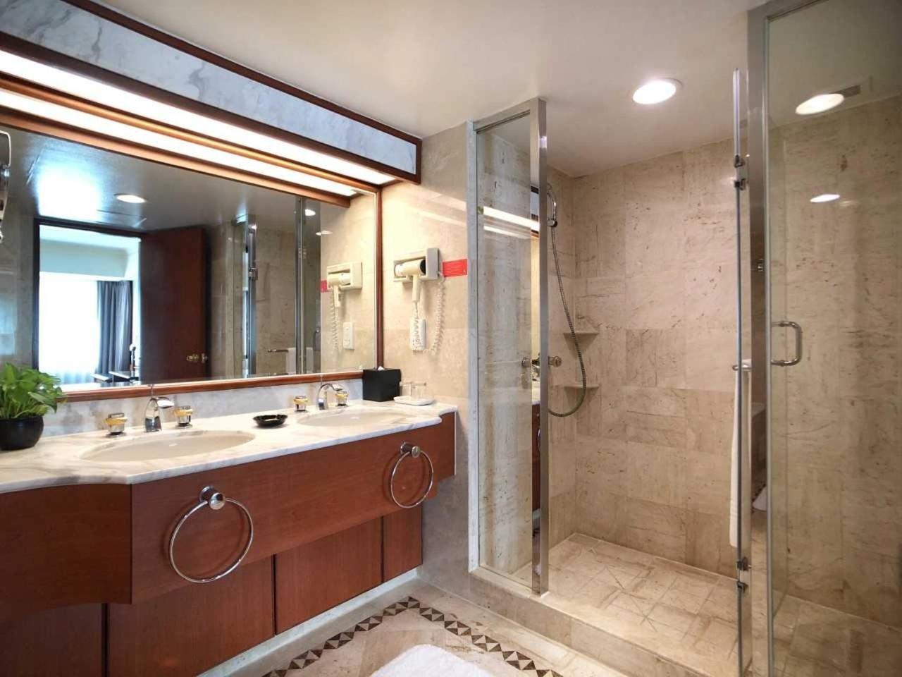 Evergreen Laurel Hotel - טאיצ'ונג מראה חיצוני תמונה The photo depicts a modern bathroom featuring a double vanity sink with a marble countertop and wooden cabinetry. Above the sinks, there is a large mirror with integrated lighting. To one side, there is a shower enclosed in glass, showcasing a sleek 