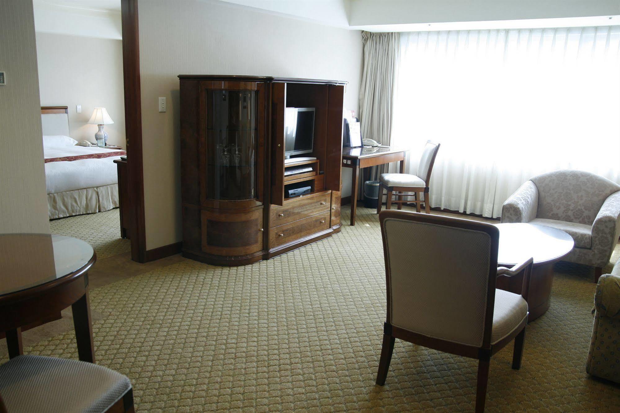 Evergreen Laurel Hotel - טאיצ'ונג מראה חיצוני תמונה The photo shows an interior of a hotel room suite. The space includes a living area with several pieces of furniture. There is a coffee table and chairs, creating a comfortable seating area. A wooden cabinet with a TV inside is situated against one w