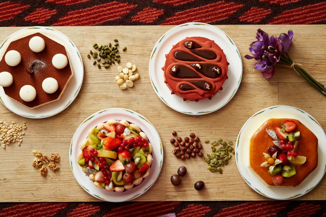 Evergreen Laurel Hotel - טאיצ'ונג מראה חיצוני תמונה The photo displays a variety of desserts arranged on small plates. There are three main cakes or tarts:

1. **Top Left Plate**: A round chocolate cake with a smooth surface and white decorations on top.
2. **Top Middle Plate**: Another cake, possibly