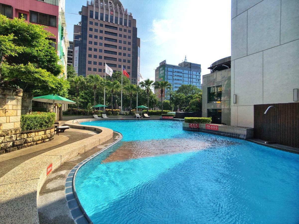Evergreen Laurel Hotel - טאיצ'ונג מראה חיצוני תמונה The photo shows a swimming pool set in a modern urban environment. The pool has a curved edge and is surrounded by greenery, including trees and umbrellas for shade. In the background, there are several tall buildings, indicating a cityscape, with so