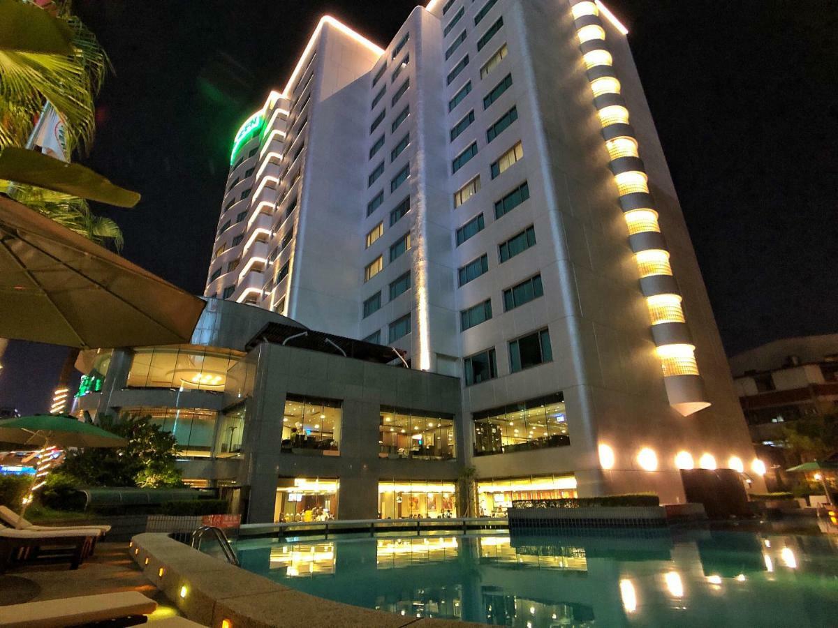 Evergreen Laurel Hotel - טאיצ'ונג מראה חיצוני תמונה The photo shows a tall hotel building at night, illuminated by lights. The architecture appears modern, with several floors and large windows. In the foreground, there is a swimming pool that reflects the lights from the building, creating a serene a