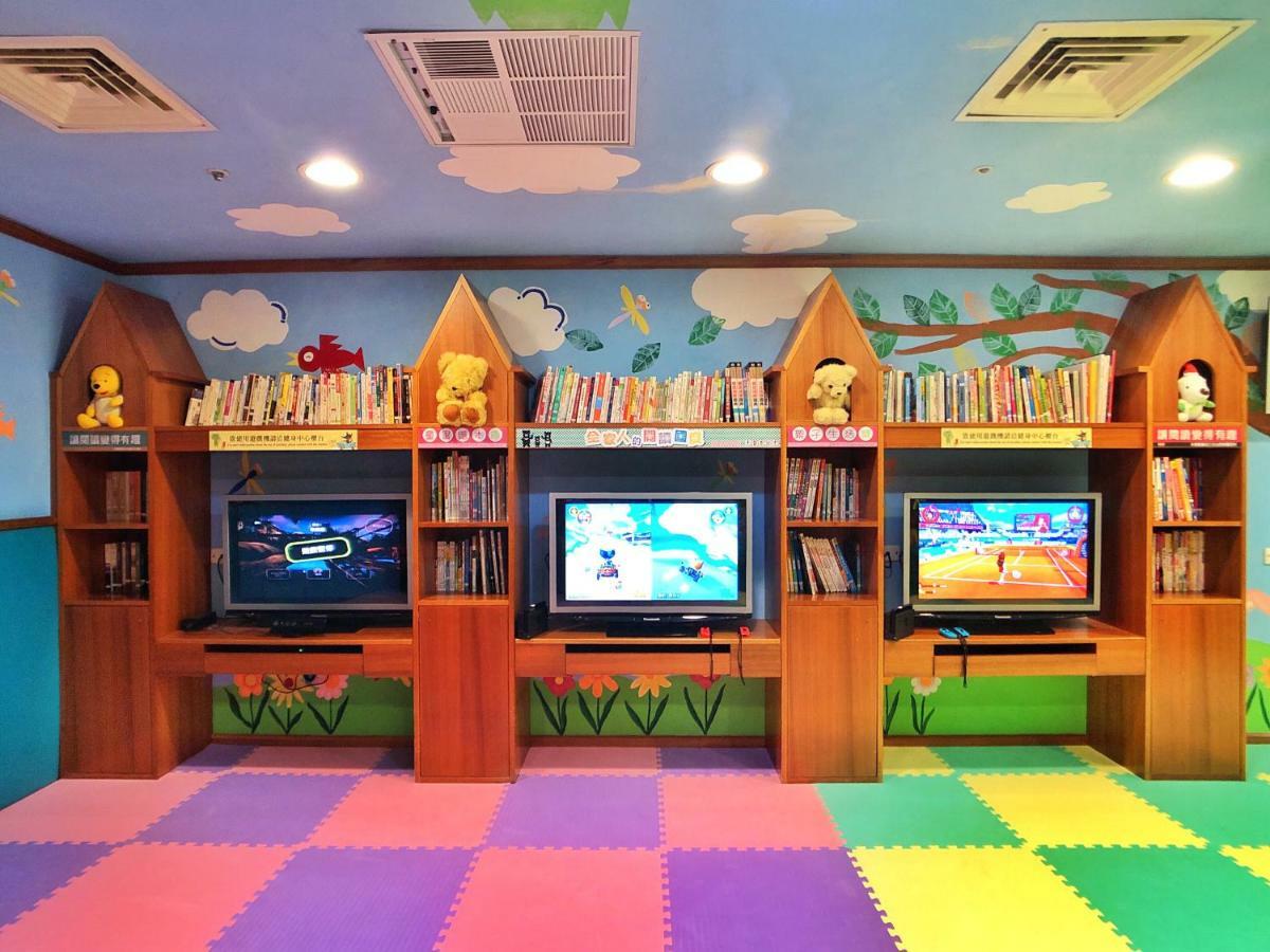 Evergreen Laurel Hotel - טאיצ'ונג מראה חיצוני תמונה The photo shows a colorful and playful room designed for children. In the center, there are three wooden gaming stations, each equipped with a television screen and surrounded by shelves filled with books. The walls are decorated with cheerful images