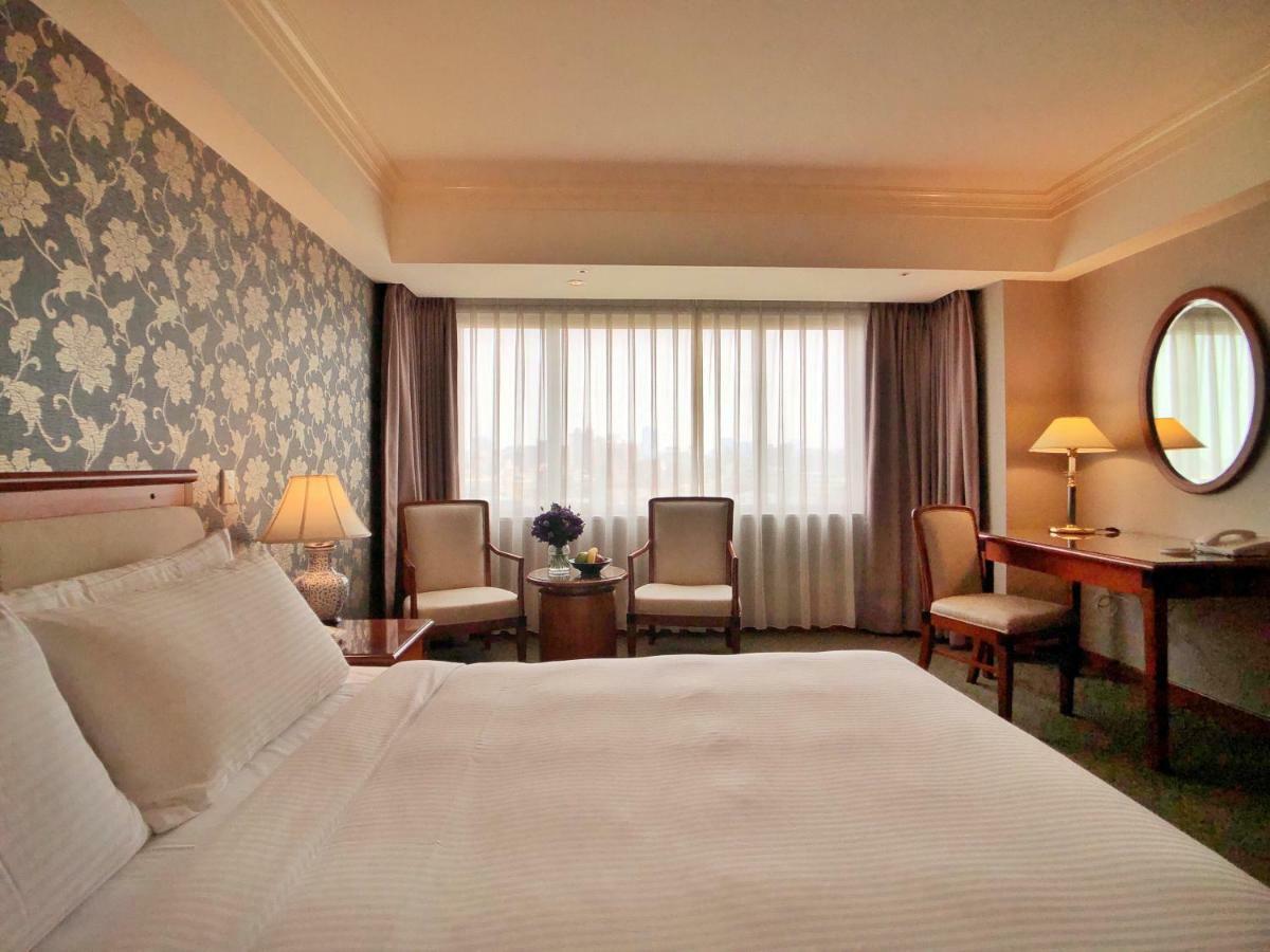 Evergreen Laurel Hotel - טאיצ'ונג מראה חיצוני תמונה The photo shows a hotel room with a comfortable and inviting design. There is a large bed with crisp white bedding on the left side of the image. To the right, there are two elegant chairs with a small round table between them, adorned with a bouquet