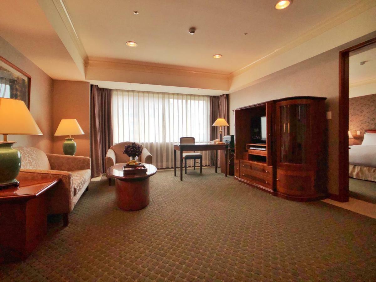 Evergreen Laurel Hotel - טאיצ'ונג מראה חיצוני תמונה The photo shows a cozy hotel suite or living area. There is a sofa and an armchair arranged around a small coffee table. A desk with a chair is positioned near a large window covered with sheer curtains that allow natural light to enter the room. Two