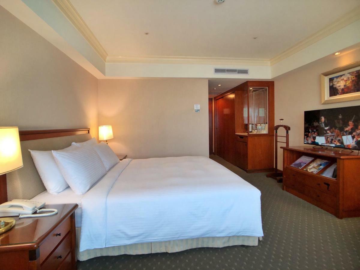 Evergreen Laurel Hotel - טאיצ'ונג מראה חיצוני תמונה The photo shows a hotel room featuring a comfortable bed with white linens and pillows, positioned against a light-colored wall. There is a wooden bedside table with a lamp and an open book next to the bed. On the opposite side, there’s a large flat-