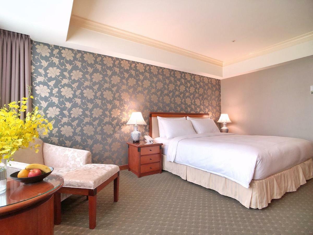 Evergreen Laurel Hotel - טאיצ'ונג מראה חיצוני תמונה The photo shows a well-decorated hotel room. It features a large bed with white bedding, situated against a patterned wall with floral designs. On either side of the bed are bedside tables with lamps. There is a small seating area that includes a cha