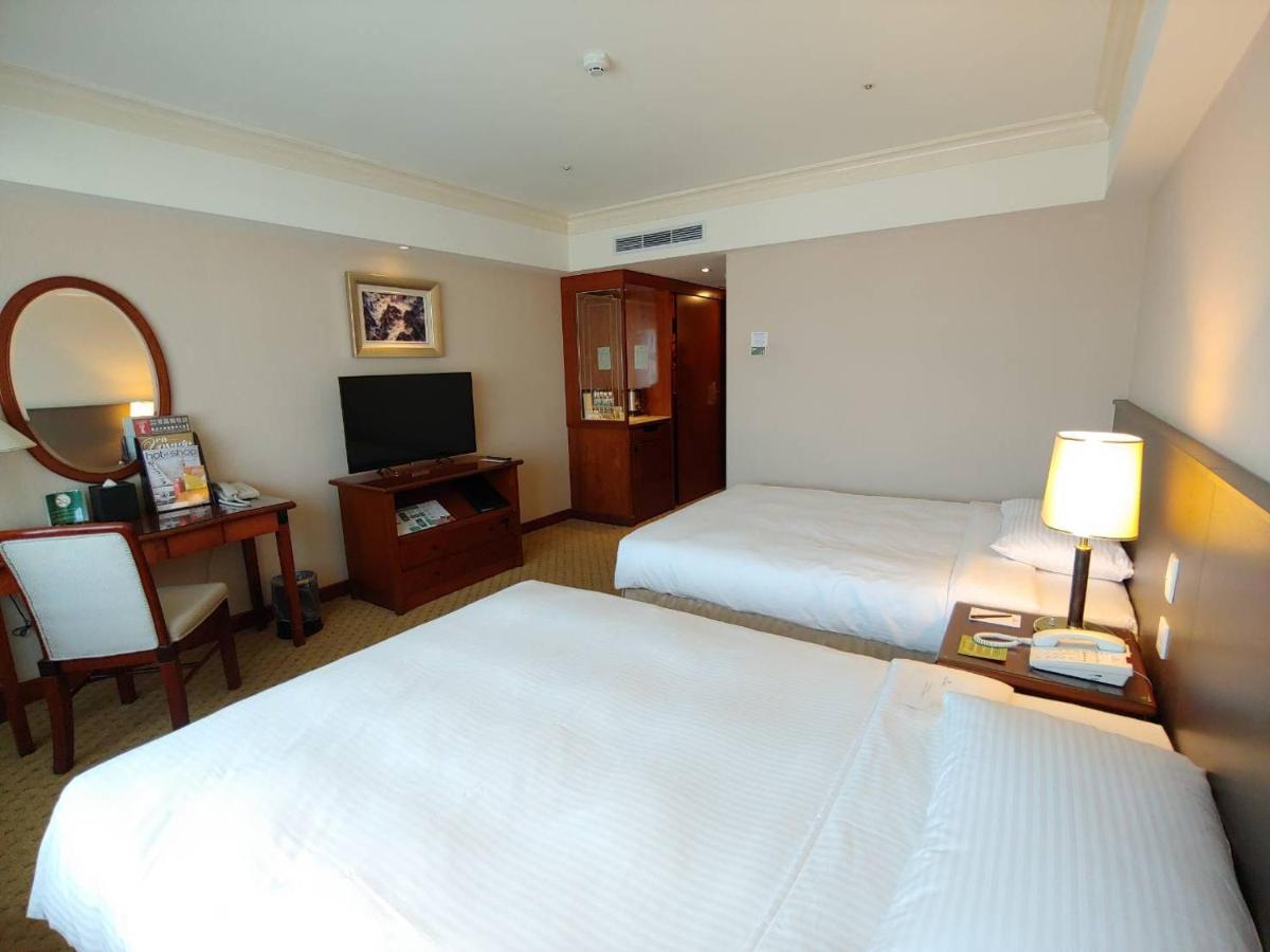 Evergreen Laurel Hotel - טאיצ'ונג מראה חיצוני תמונה The photo shows a hotel room with two beds, neatly made with white linens. There is a desk and chair in one corner, accompanied by a flat-screen TV mounted on the wall. A large mirror and a wooden cabinet are also visible. The room is illuminated by 